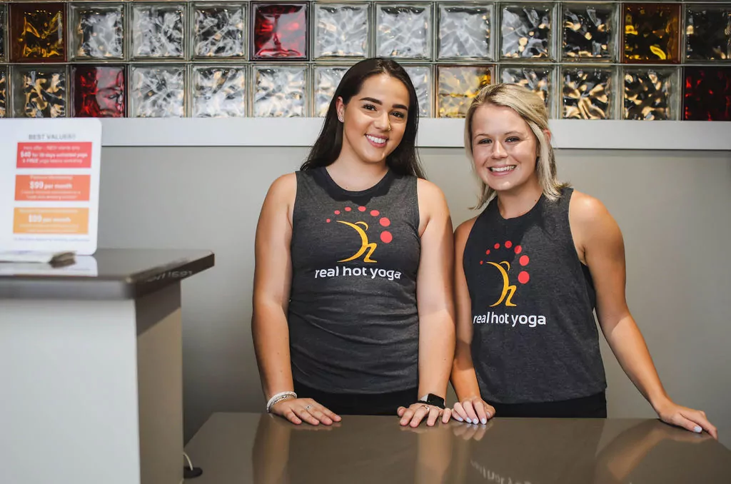 Two Smiling Girls Behind the Reception Desk in Real Hot Yoga Tank Tops